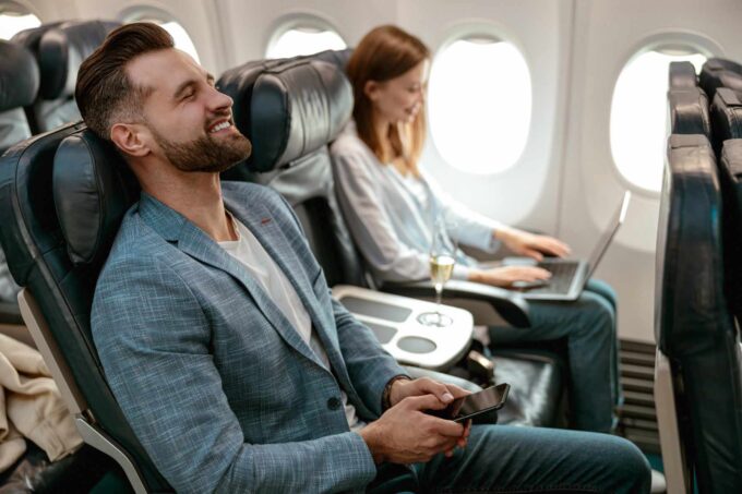 Radosny, brodaty mężczyzna ze smartfonem podróżujący samolotem