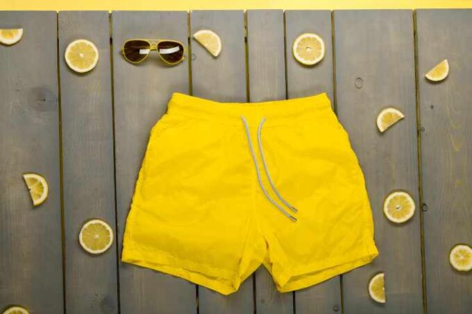 Akcesoria plażowe w tle. Żółty strój kąpielowy jednoczęściowy, szorty kąpielowe.