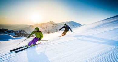 Mężczyzna i kobieta zjeżdżający na nartach o zmierzchu, ośnieżona góra w tle